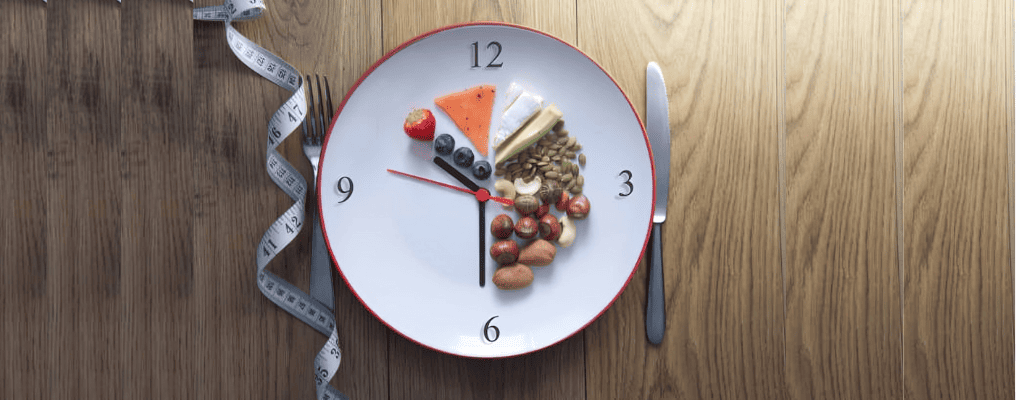White plate styled as a clock with nuts and healthy foods, surrounded by measuring tape, fork, and knife